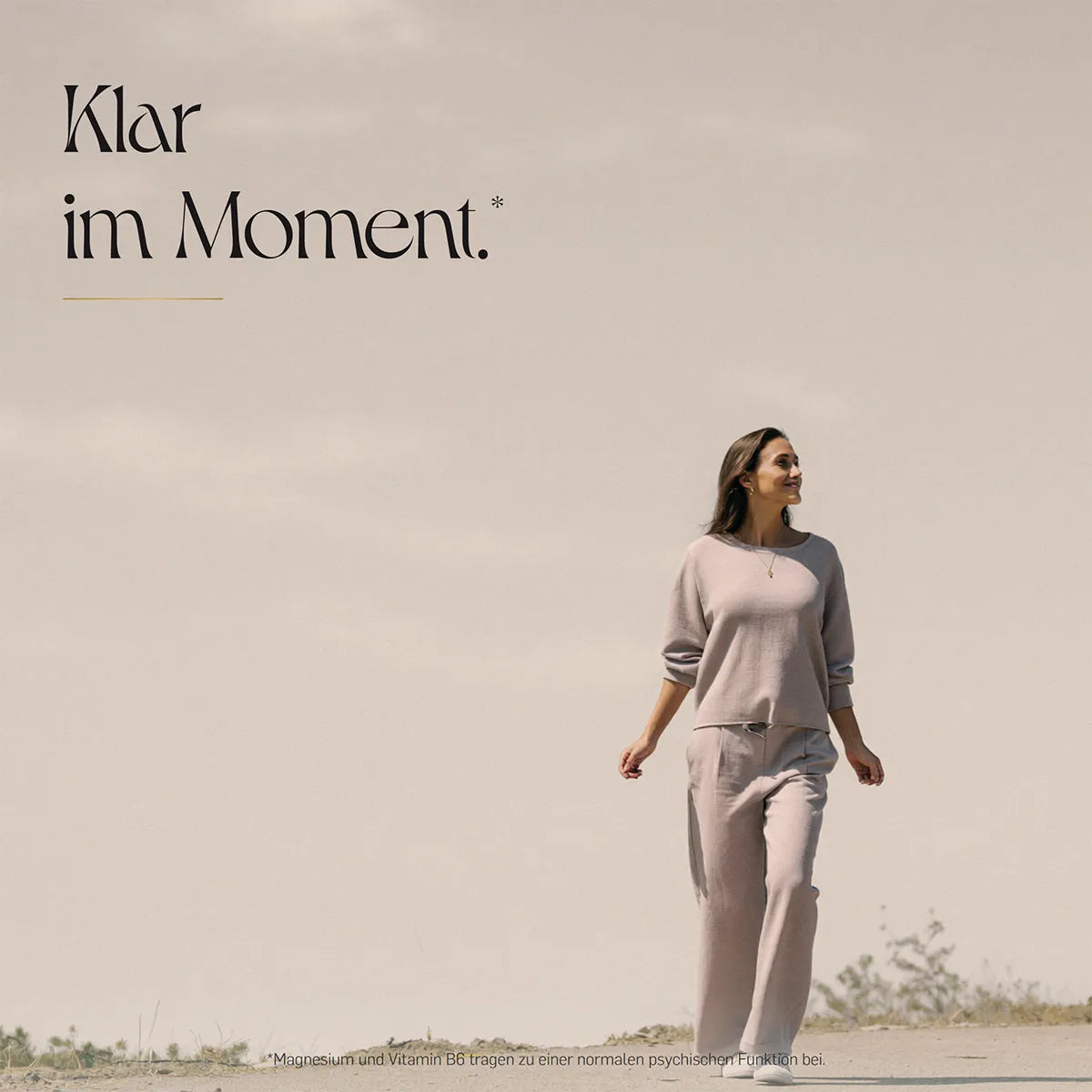 Klar im Moment – Frau in beigem Outfit geht entspannt durch eine helle Dünenlandschaft mit vereinzelten Gräsern unter weitem Himmel.