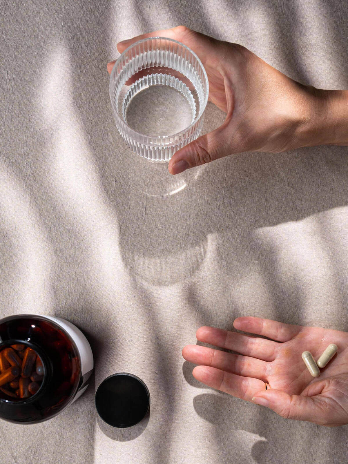 Hand hält Glas Wasser und zwei Bio Brahmi Kapseln von Kurkraft auf hellem Stoffuntergrund