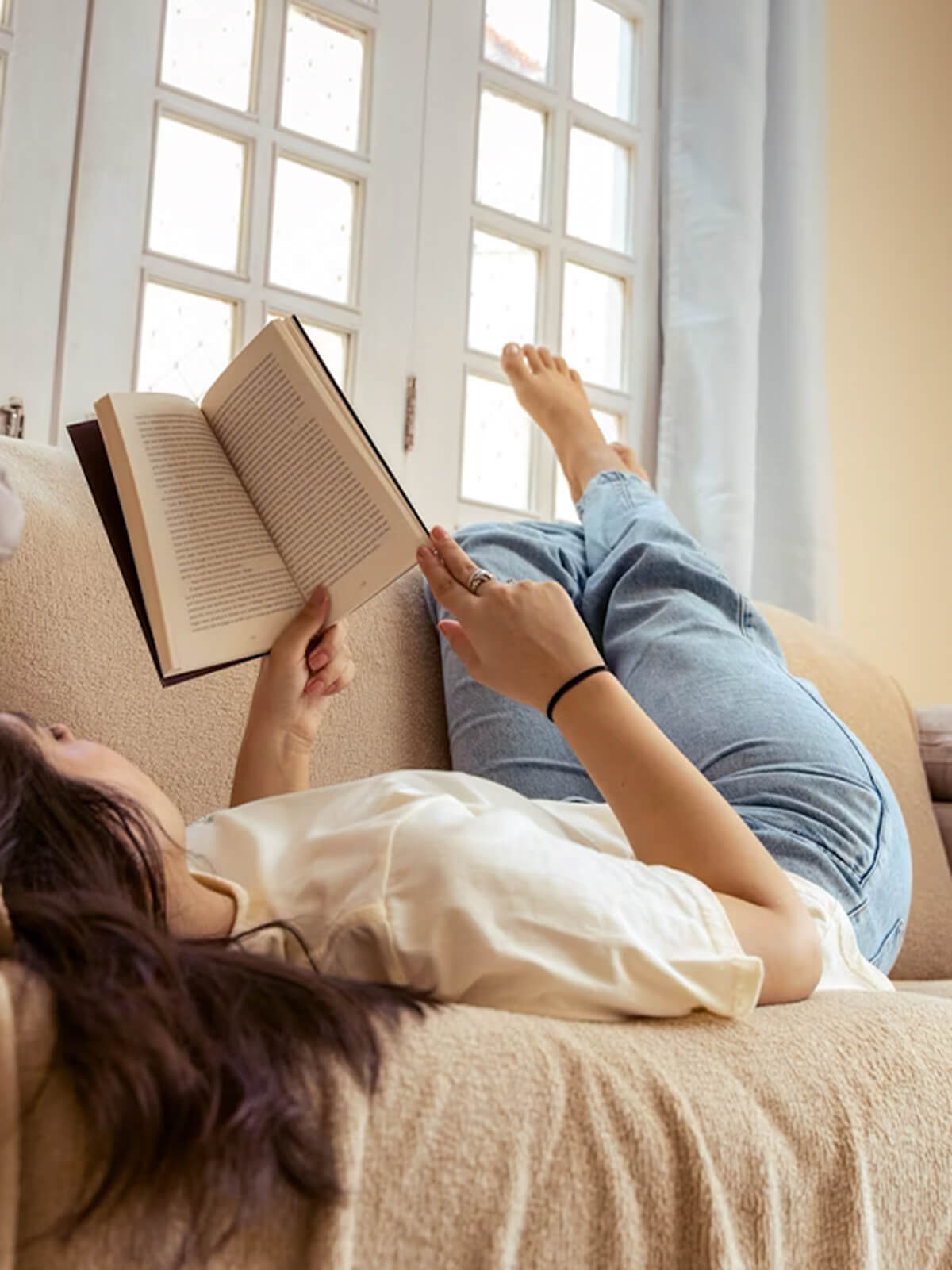 Frau liegt entspannt auf dem Sofa und liest ein Buch – ruhiger Moment mit Vitamin B Komplex von Kurkraft