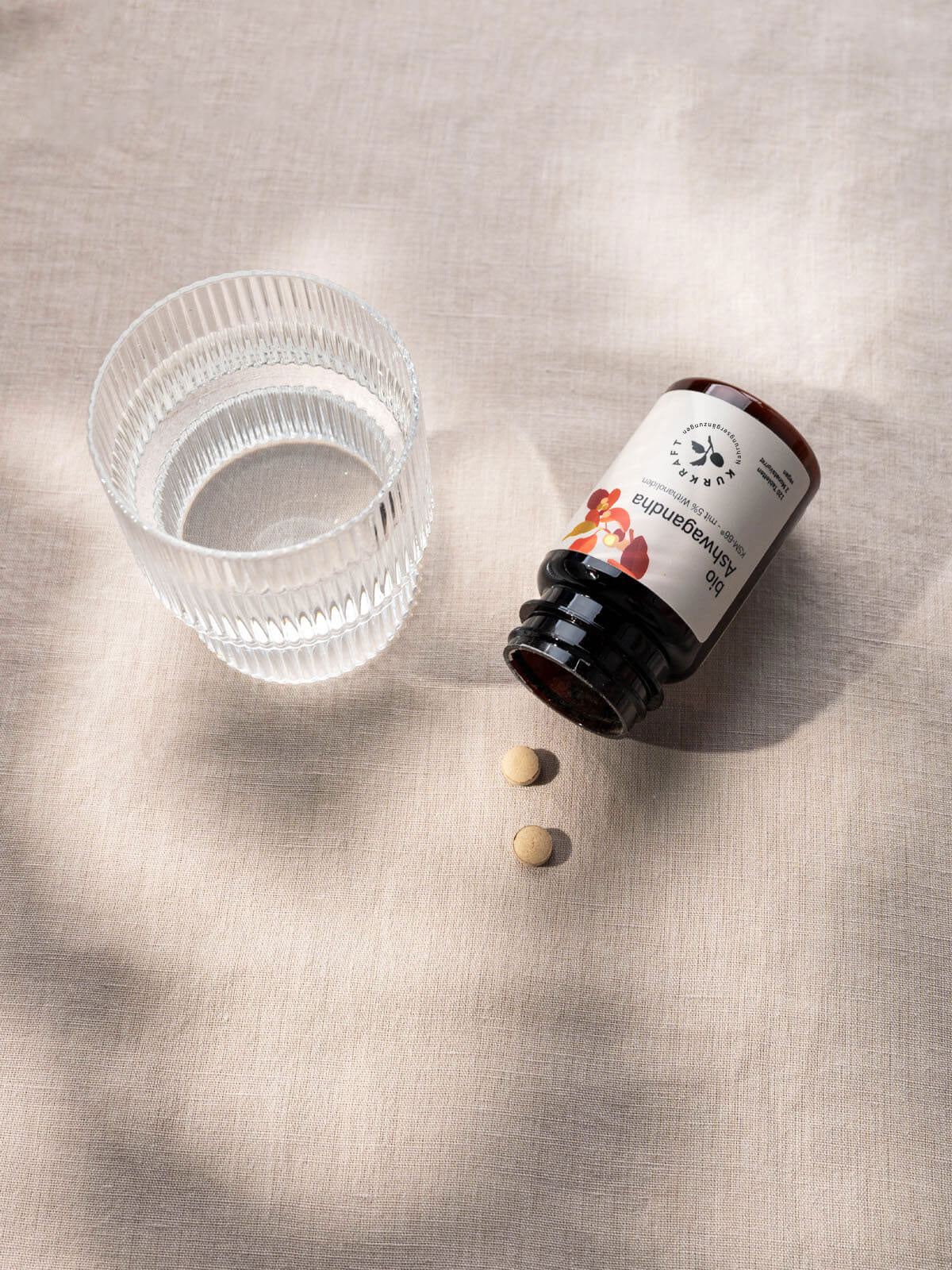 Bio Ashwagandha KSM-66 Tabletten von Kurkraft neben einem Glas Wasser auf hellem Leinentuch.