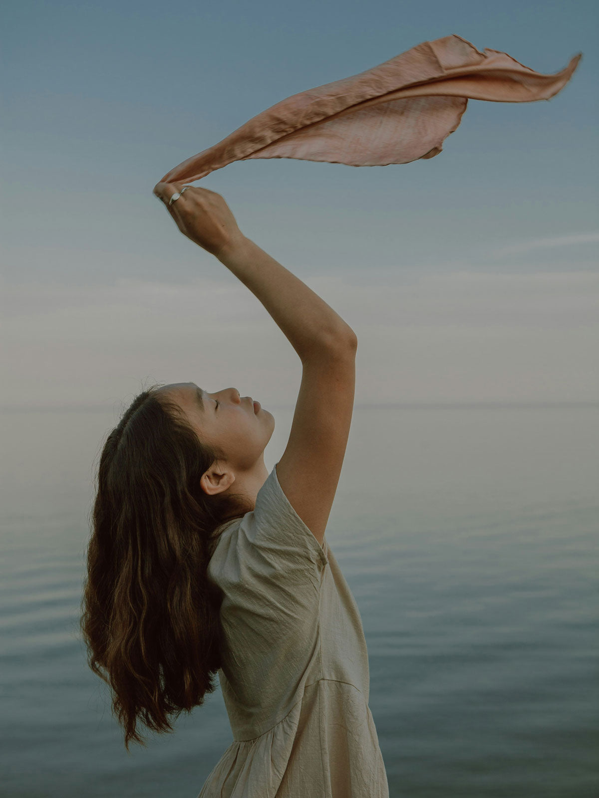 Frau am Meer hebt ein Tuch in die Luft – Sinnbild für Leichtigkeit und natürliche Balance mit Kurkraft OPC Traubenkernextrakt Kapseln.