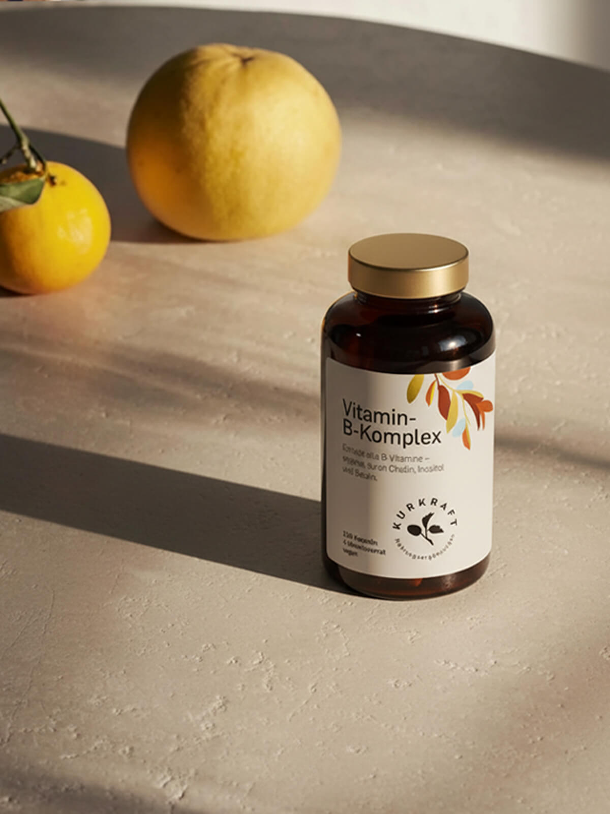 Vitamin B Komplex in brauner Dose mit goldfarbenem Deckel auf heller Fläche, im Hintergrund frische Zitrusfrüchte