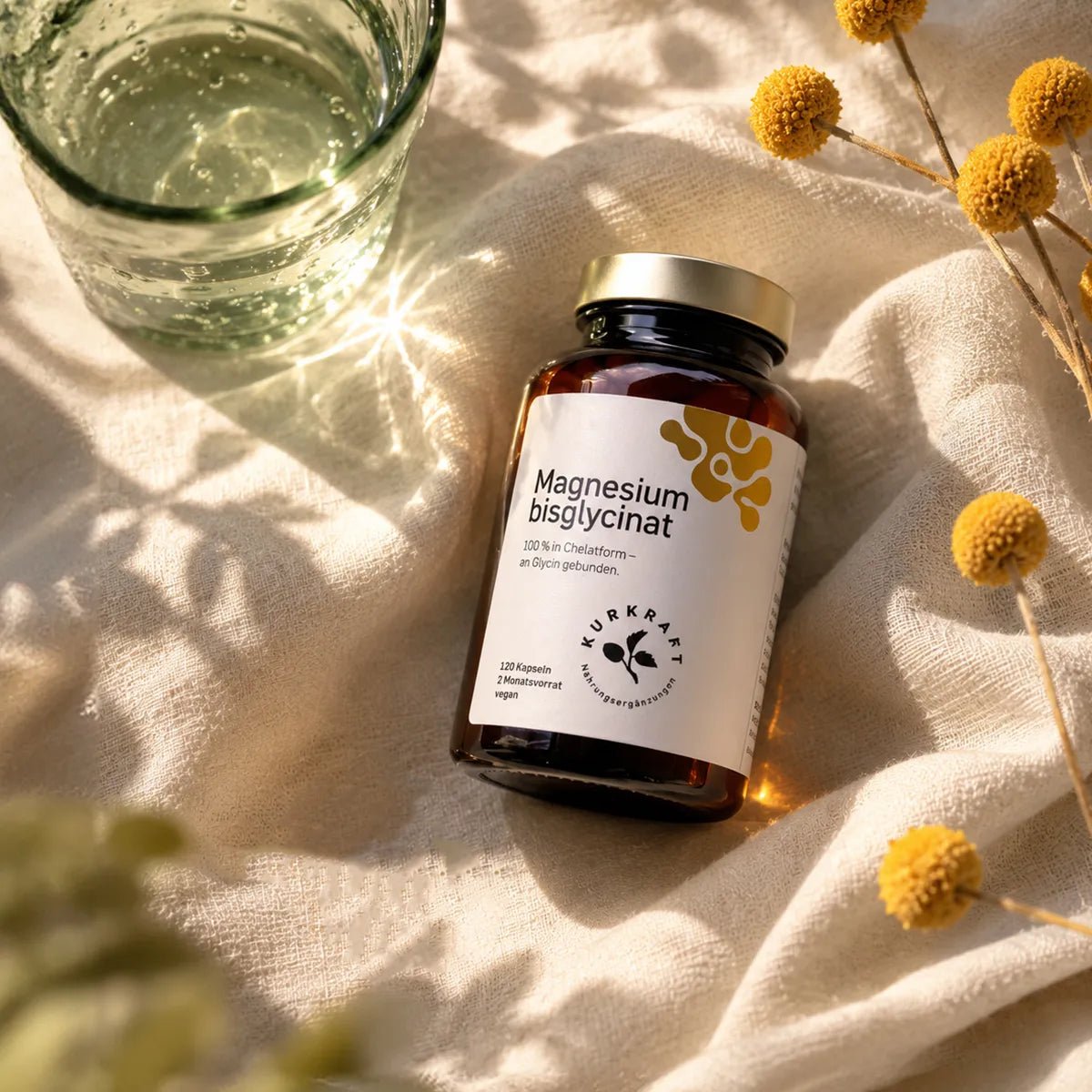 MAGNESIUM BISGLYCINAT - Kurkraft - Magnesium Bisglycinat von KURKRAFT kaufen: Dose mit Schraubdeckel im Sonnenlicht auf Leinen, Wasserglas und getrocknete Gelbblüten.